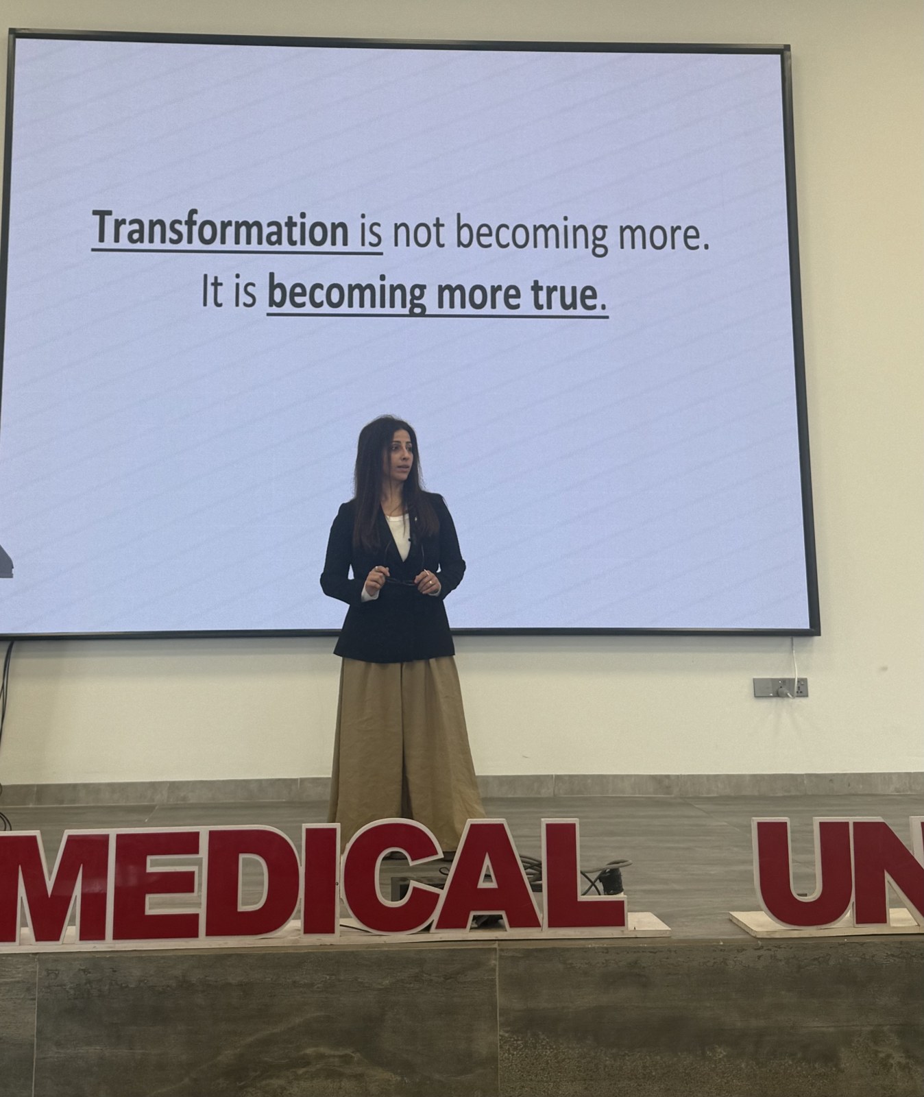 Banu speaking at Hawler Medical University, 2026, in front of the slide: Transformation is not becoming more. It is becoming more true.